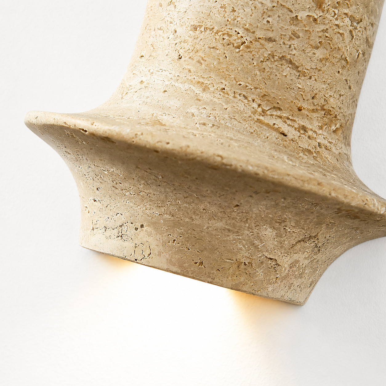Lit close view of travertine wall lamp showing warm downward glow and honed stone edge