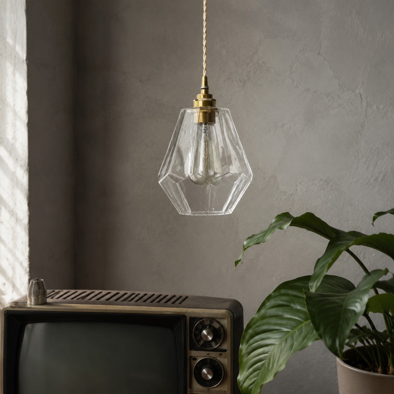 Faceted glass pendant light hanging near a vintage television and plant
