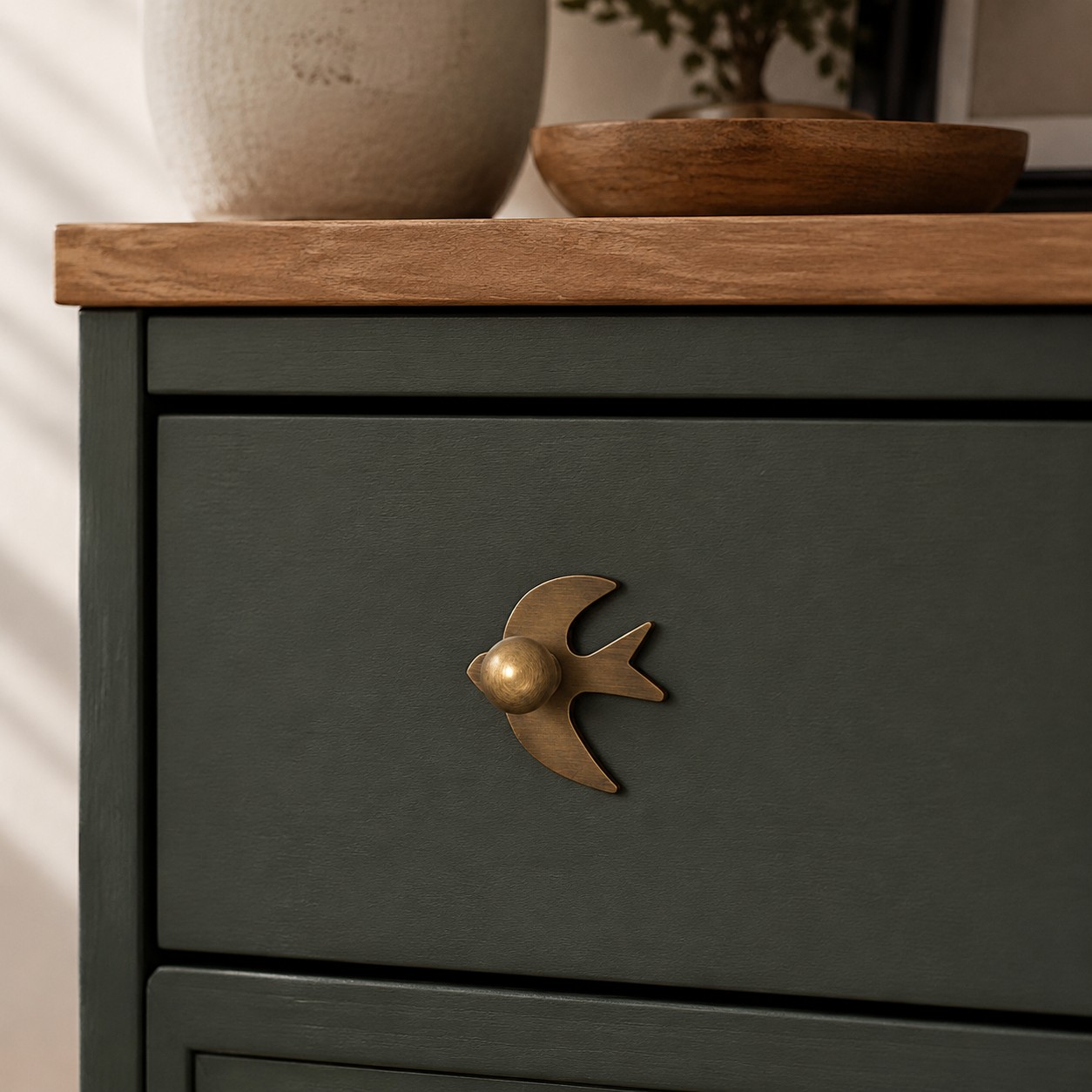Antique brass swallow cabinet knob on a dark green drawer
